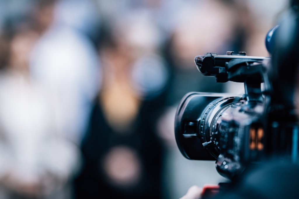 A person holding a video camera in front of a crowd.