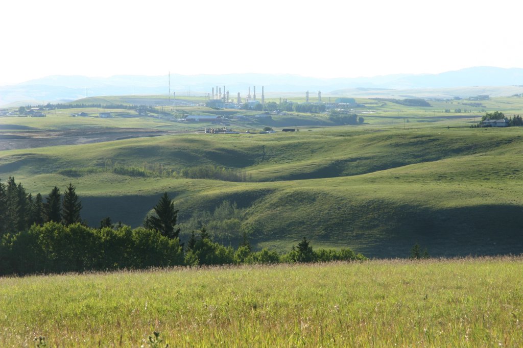 Oil refinery Gas plant in distance with rolling green Foothills in Foreground.