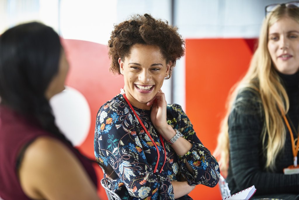 A group of women smiling, in a conference room discussing internal communications strategies.